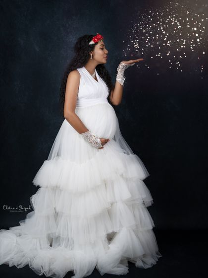 Blowing a little magic. This whimsical shot features a mom-to-be in a white ruffled gown, blowing sparkling glitter for a fairytale effect.