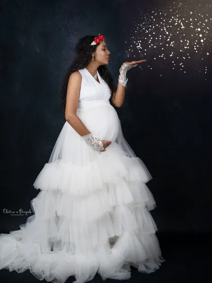 Blowing a little magic. This whimsical shot features a mom-to-be in a white ruffled gown, blowing sparkling glitter for a fairytale effect.