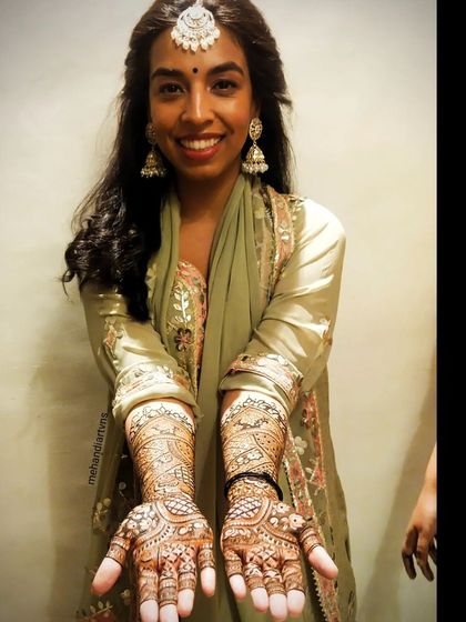 A happy client showing off her full-arm traditional mehandi. The design is dense and detailed, perfect for a wedding celebration.