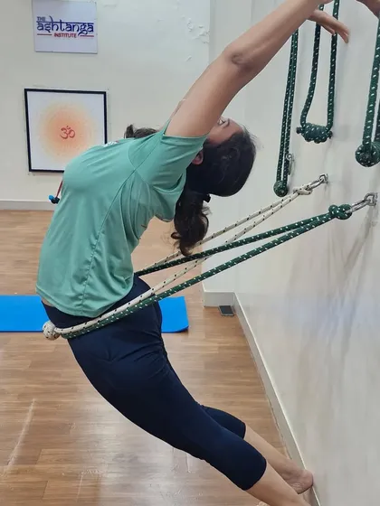 A student performs a deep backbend using the rope wall for support. This prop-assisted Urdhva Dhanurasana variation helps open the chest and shoulders while protecting the lower back, making the pose more accessible.