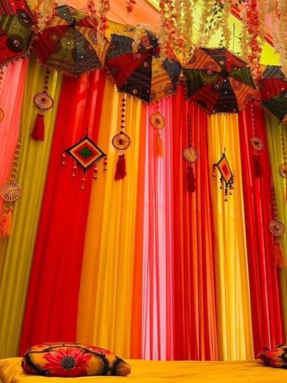 I love using colorful props to enhance the decor. This Mehandi seating features a backdrop of bright drapes decorated with hanging Rajasthani umbrellas and traditional tassels.
