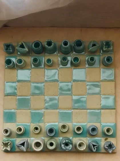 An overhead view of the 'Cocoa Clash' handmade ceramic chess set. The board and all 32 pieces are crafted from clay.