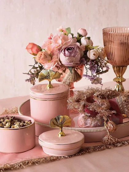Our Festive Treasure Hamper is a beautiful collection in pink. It includes a large candle, a potli of trail mix, flower decor, and jars of mini cookies and pan berry flakes.