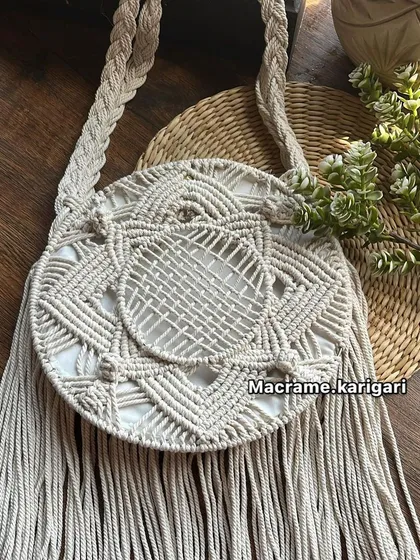 This round macramé bag in a muted beige tone is perfect for achieving an earthy, bohemian look. The intricate knotting and fringe detail add a touch of artisanal craftsmanship.