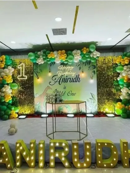 A grand jungle-themed first birthday on a stage, with large light-up letters spelling the name "ANIRUDH" and a custom backdrop.