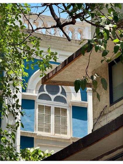 A beautiful blue and white heritage building in Kala Ghoda, its arched window peeking through the leaves.