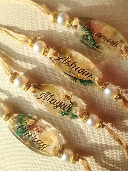 The sunlight catching these custom name rakhis really shows off the details inside. You can see the delicate green leaves and tiny flowers preserved perfectly in the resin, making each handmade rakhi a small piece of art.