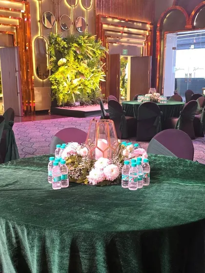 A simple and elegant table setup with a floral centerpiece and a candle lantern on a green velvet tablecloth.