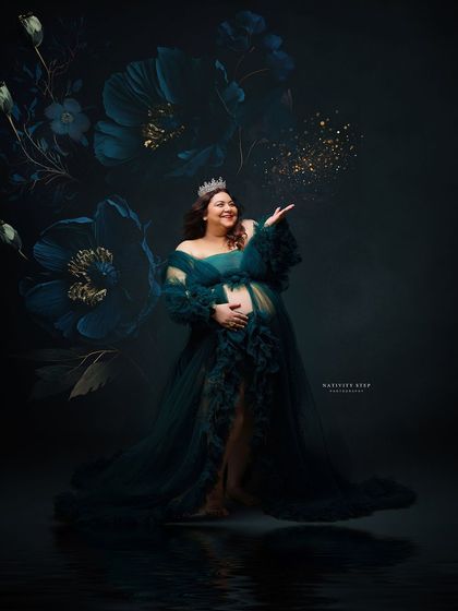 A joyful and glamorous shot of a mother-to-be in a teal gown, blowing glitter. The added crown and floral backdrop create a celebratory and magical atmosphere.
