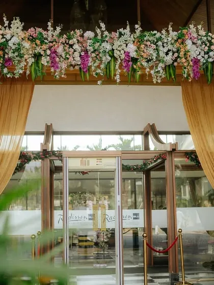 I used a combination of colorful flowers and rich golden drapes to create a warm and inviting entrance arch for this event, perfectly complementing the venue's modern glass doors.
