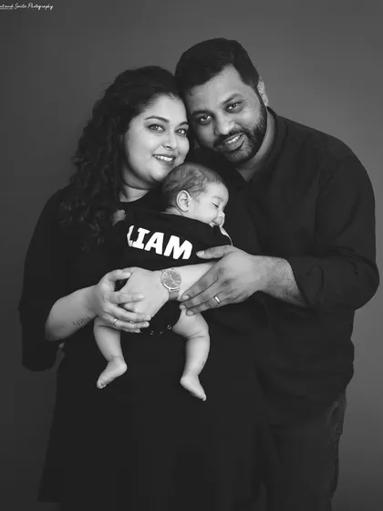 A classic black and white family portrait with a newborn. The focus is entirely on the family's happy expressions as they hold their newest member.