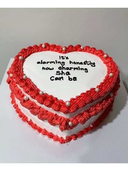 A vintage-style heart-shaped cake in red and white. The detailed piping and pearl accents give it a charming, classic look.