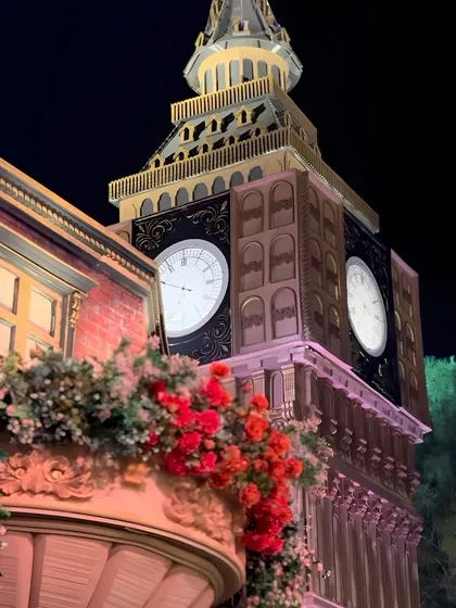 A detailed shot of the Big Ben replica, showcasing the intricate architectural work and the vibrant red flowers adorning the balconies of the adjoining structures, blending London's grandeur with celebratory flair.