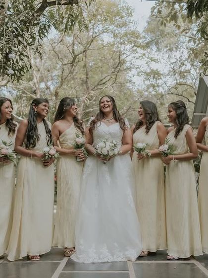 A bride shares a laugh with her bridesmaids. The stone-paved courtyard and overhanging trees create a relaxed and beautiful setting for group photos.