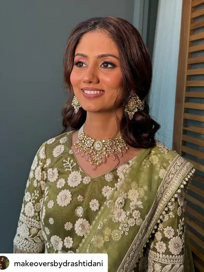 A smiling shot of the bride. Her makeup is fresh and luminous, with soft pink tones on her cheeks and lips to complement her lovely green outfit.