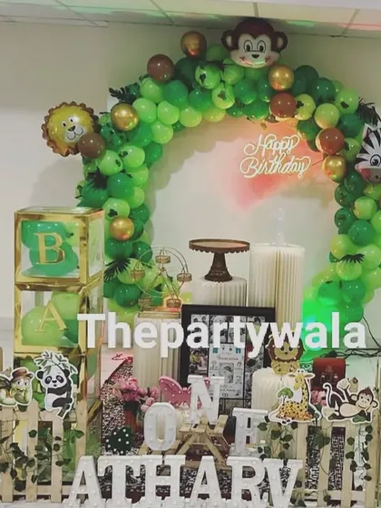 A cute jungle theme with a neon "Happy Birthday" sign. The green balloon arch is decorated with monkey and zebra foil balloons.