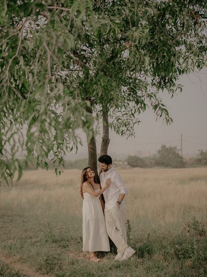A candid and happy interaction under a tree, showcasing the couple's easy comfort and love in a natural setting.