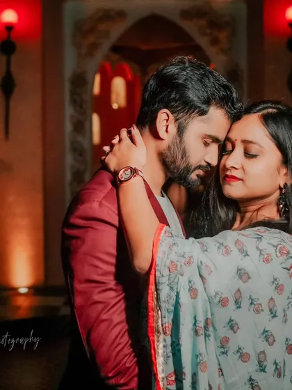 An intimate embrace in a room with warm, moody lighting. The red tones of the lights and the groom's jacket add a touch of passion to this romantic close-up.