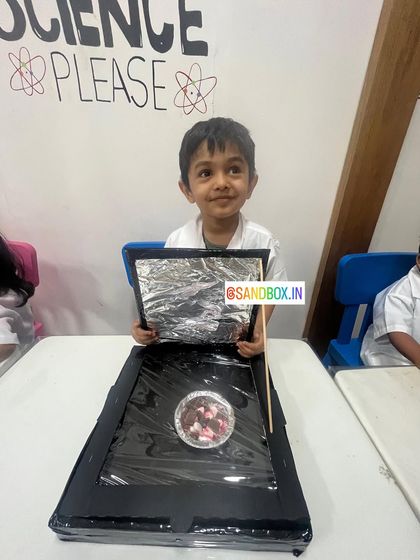 This little chef is ready to test out his solar cooker. We placed some marshmallows inside to see how effectively the sun's rays could melt them, a delicious experiment in thermal energy.
