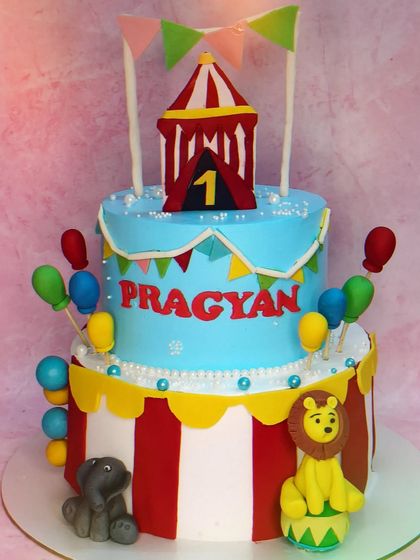 Welcome to the circus! This two-tier first birthday cake features two different flavors, pineapple and chocolate, to please every guest. The handmade fondant animals and circus tent topper create a fun and festive atmosphere.