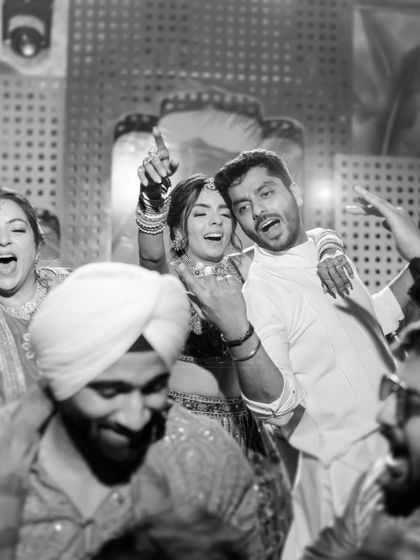 The raw energy of the Mehendi party captured in a candid black and white shot, showing the couple and guests dancing without inhibition.
