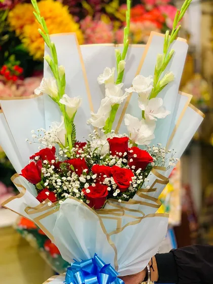 A closer look at the red rose and white gladiolus bouquet, showing the delicate baby's breath filler and the crisp lines of the wrapping.