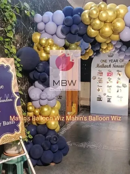 A royal first birthday bash for a little prince. The entrance features a grand balloon arch in navy, periwinkle, and gold, with a personalized welcome sign.