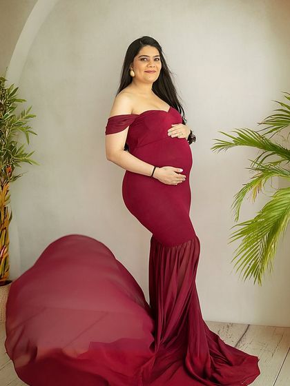 A full-length portrait showcasing a stunning mermaid-style red gown with a dramatic train. The off-shoulder design is elegant and flattering.