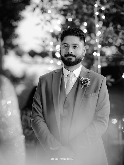 A classic black and white portrait of the groom, Richard, waiting for his bride. The soft focus and bokeh from the lights create a timeless and romantic mood.