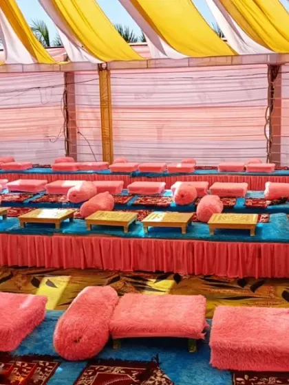 A traditional floor seating arrangement I organized for a large gathering or langar. The setup includes low wooden tables (bajots) with pink cushions for guests, all arranged neatly under a draped pandal.