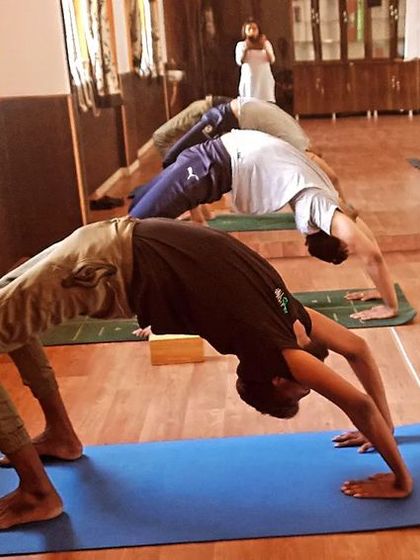 Students practicing Chakrasana (Wheel Pose) in a group setting. This advanced backbend opens the chest, stimulates the endocrine system, and builds confidence.