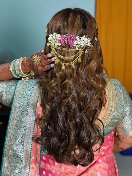 A beautiful hairstyle with open curls and a floral hair accessory, perfect for a Mehendi or Haldi event.