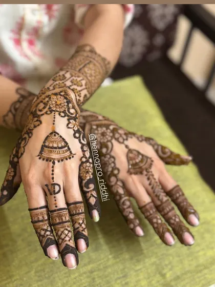 An elegant back hand design featuring a hanging jhumka motif and a personalized initial. This style is a favorite among bridesmaids and family members for its grace.