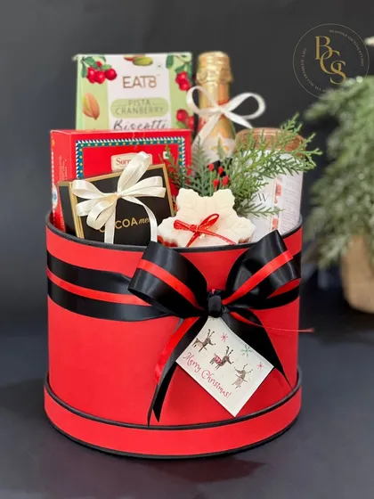 A luxurious Christmas hamper in a festive red hatbox, perfect for making a grand statement. It’s filled with premium items, including a small bottle of champagne.