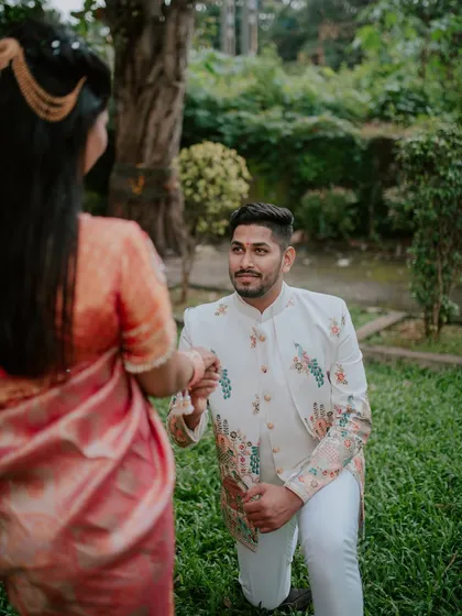 The groom-to-be on one knee, presenting the ring during an outdoor engagement photoshoot.