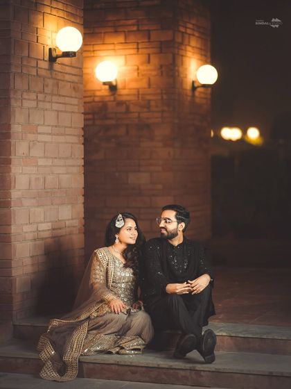 An intimate moment during a Sangeet night. The couple shares a quiet conversation under the warm glow of wall lights, a peaceful pause in the middle of the celebration.