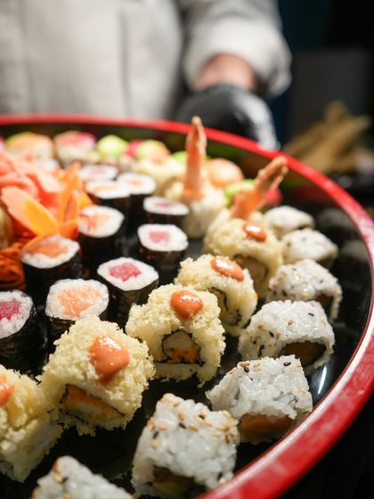A chef holds a freshly prepared party platter, showcasing the abundance and variety we offer. This platter includes tempura prawn rolls, classic maki, and other favorites.