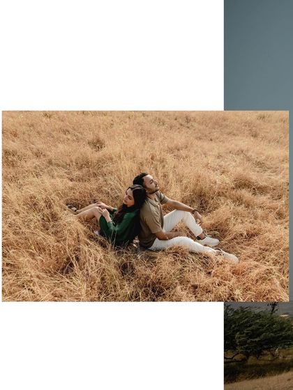 A serene moment of the couple sitting back-to-back in a field of golden grass. It's a peaceful, contemplative shot about being together in nature.