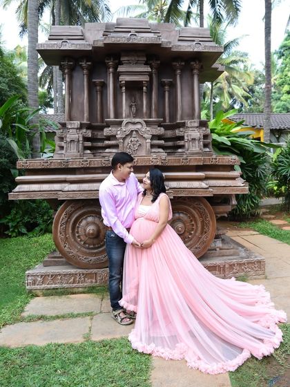 A grand outdoor portrait of a couple in front of a stone temple chariot. The mom-to-be's pink gown adds a soft, romantic touch to the impressive backdrop.