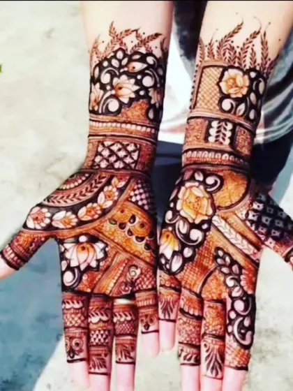 A beautiful henna design with a rich brown stain, perfect for outdoor events. The pattern includes floral motifs and delicate leafy vines at the top of the arms.