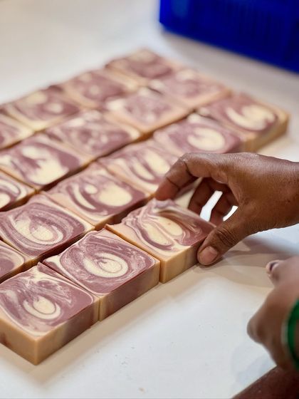 A hand reaching to adjust the freshly cut Sweet Rose soaps. Each bar is inspected before moving on to the stamping and wrapping stage.