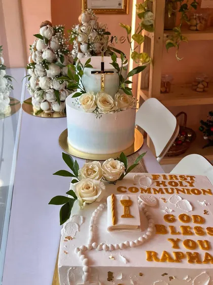Another angle of our beautiful Communion cakes. You can see the detailed piping on the square cake and the delicate floral arrangements on the round tiered cake, all ready for a blessed celebration.