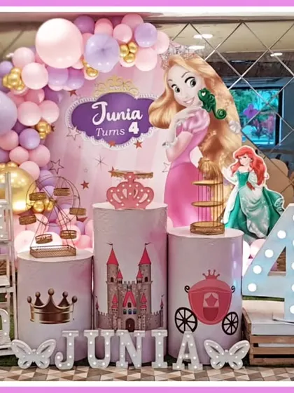 A grand princess-themed fourth birthday party. This setup features cutouts of various Disney princesses like Rapunzel and Ariel, a castle-themed backdrop, and a large light-up number '4'.