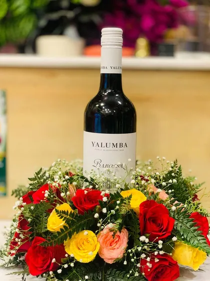 A clear shot of the wine bottle arrangement, perfect for an anniversary or formal event. The mix of red, yellow, and pink roses beautifully complements the bottle.