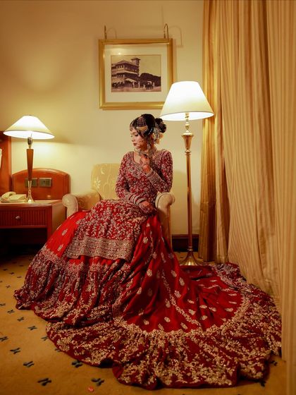 A full-length shot of the bride seated, showcasing the magnificent trail of her red lehenga. The entire look is one of regal elegance.