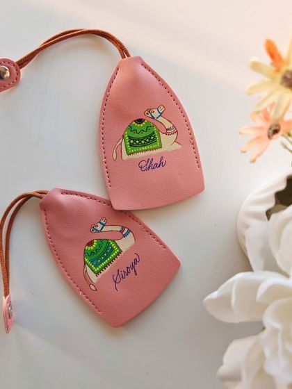 A pair of pink leather keychains, personalized with the names 'Kiroya' and 'Shah' alongside the camel illustration.
