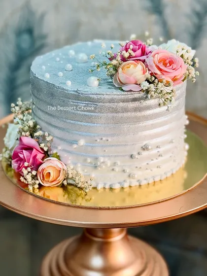 A stunning silver-dusted tall cake for a 25th wedding anniversary. The metallic sheen combined with fresh flowers and delicate pearls creates a sophisticated and celebratory feel.