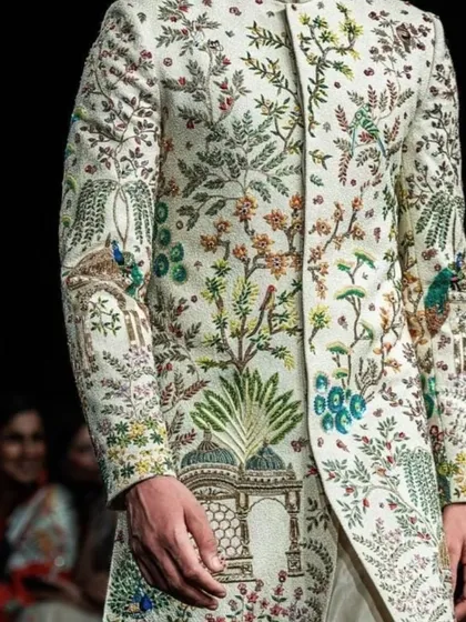 A close-up of a runway sherwani featuring multi-color, all-over embroidery depicting a lush garden scene with peacocks. This is the pinnacle of bespoke bridal couture for men.