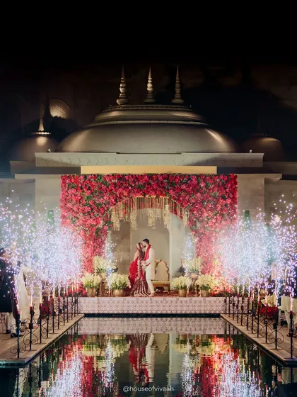 The moment of union, framed by a wall of red roses and the architectural splendor of Fairmont Jaipur. The reflection in the water adds a layer of magic to this perfectly symmetrical and powerful shot.