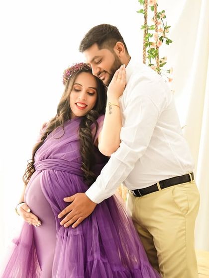 A tender moment captured between the expecting couple. The soft lighting highlights the texture of the purple ruffled gown and the gentle embrace.